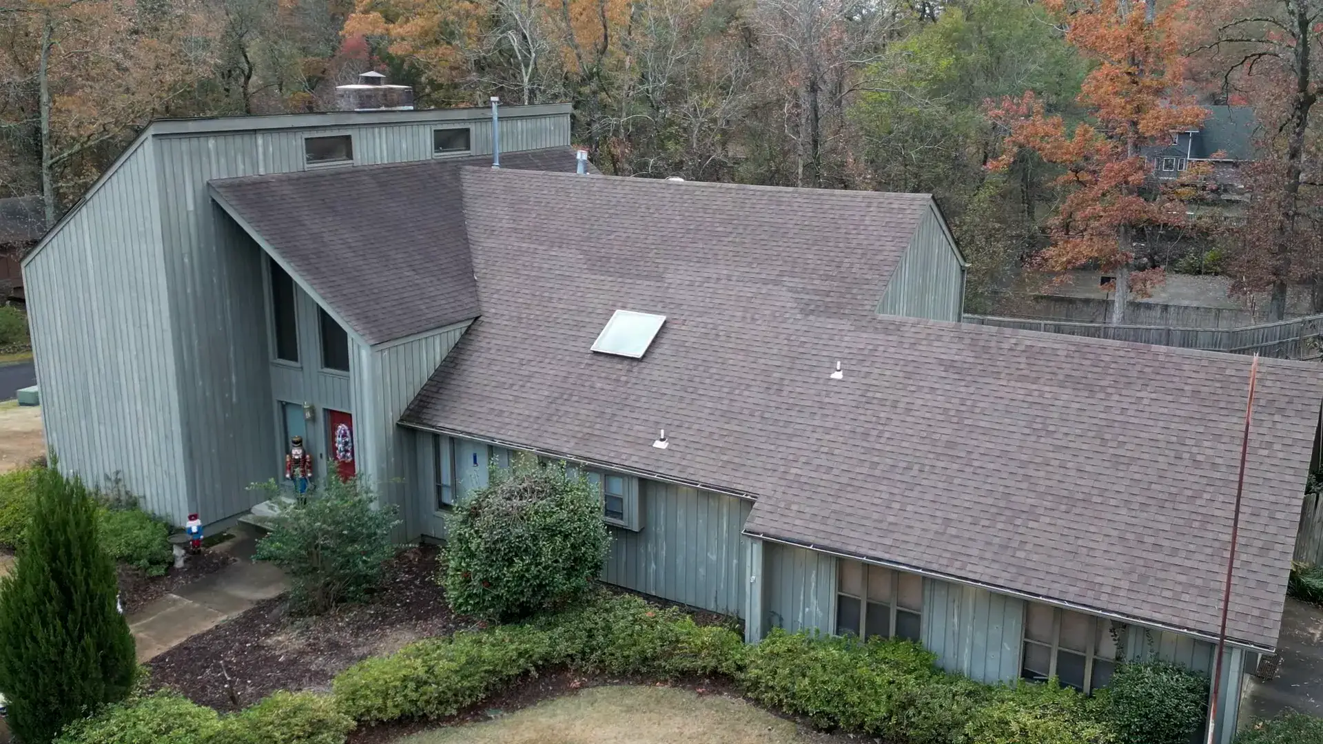 Large wooded Arkansas home with a freshly completed shingle roof surrounded by autumn trees